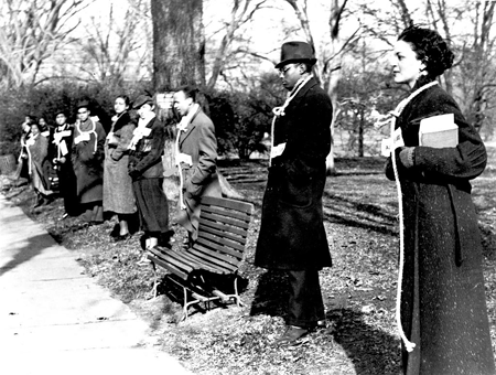Black-and-white photo of students in winter coats standing along a sidewalk in silent protest, each with a rope dangling from their neck suggesting a lynching noose.