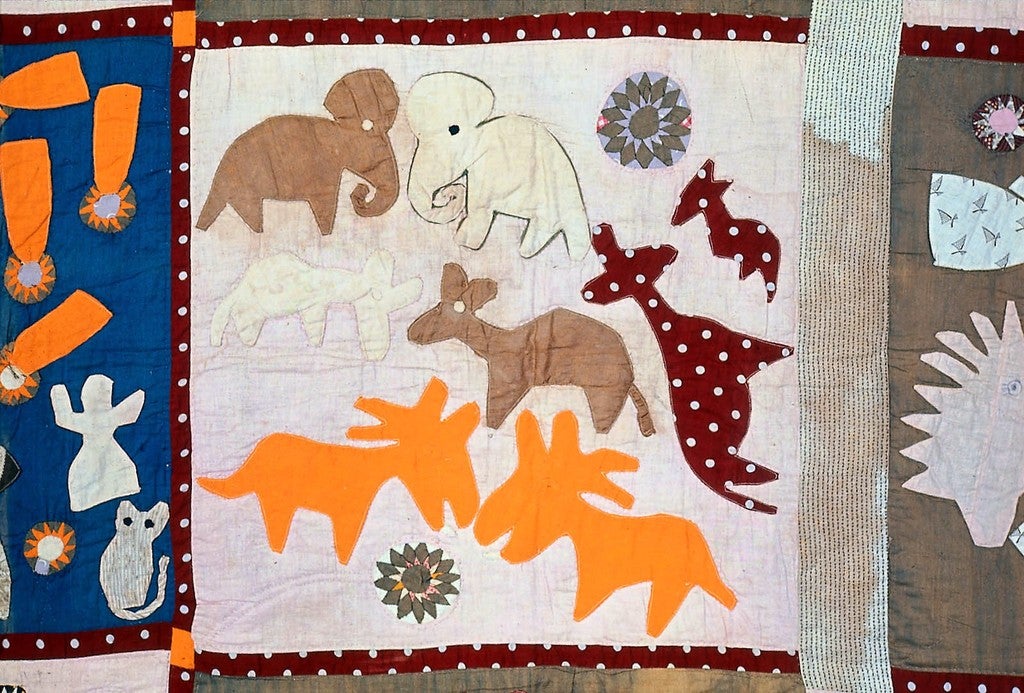 Detail of a colorful quilt block with appliques of elephants, antelopes, and other African animals on a pale background.