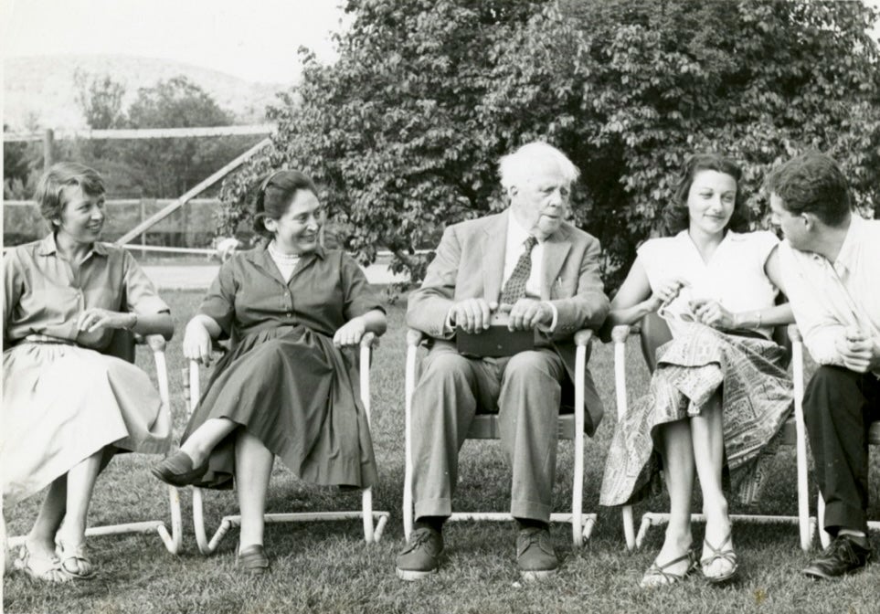 Black-and-white photo of an older man in a suit sitting outdoors with four younger people, all smiling and talking while seated in folding chairs on a lawn.