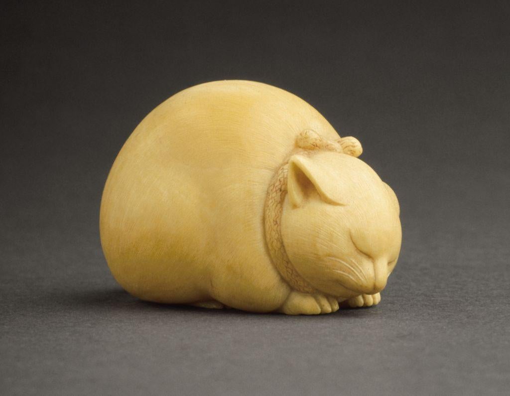 Small carved figure of a curled, sleeping cat with tucked paws and closed eyes.