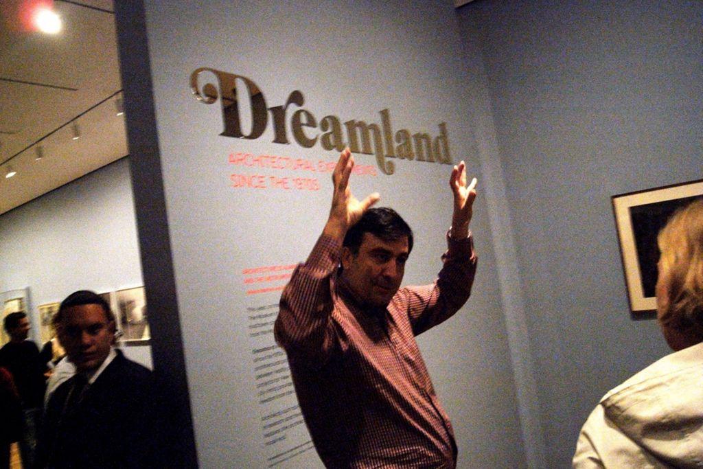 A person gesturing animatedly in front of a museum wall with the exhibition title “Dreamland” displayed in metallic lettering.