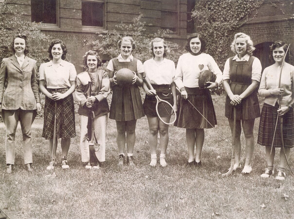 Women in various sports uniforms stand in a line, holding items like golf clubs, tennis rackets, and more.