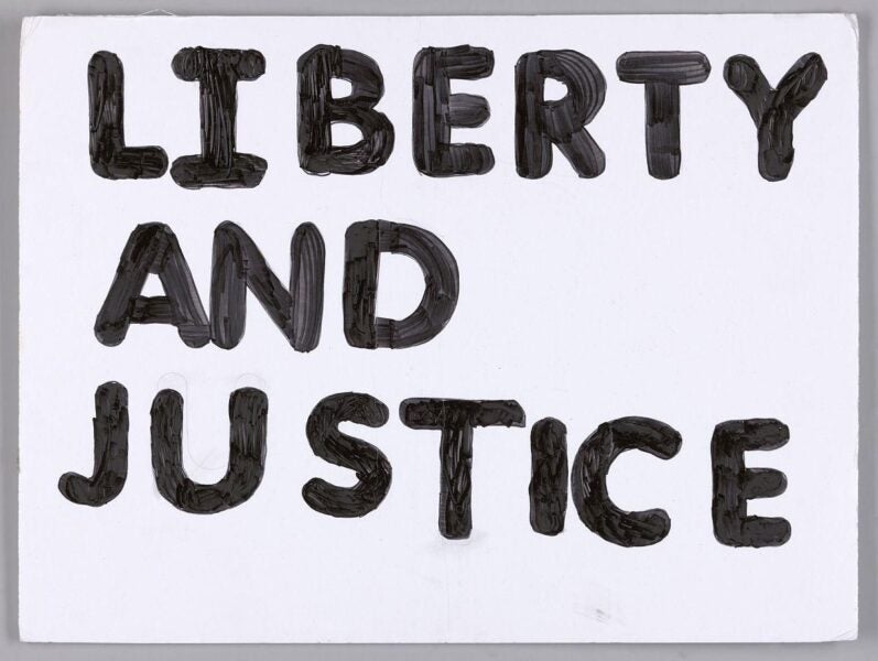 Black, painted text on a white poster board that reads ‘LIBERTY AND JUSTICE’.
