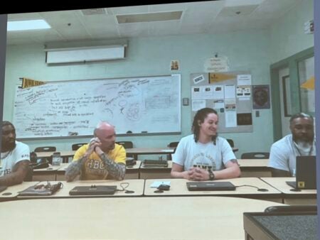 Four men wearing Bowie University tee shirts are sitting in a computer lab at Jessup Correctional Facility. They are using their Orijin zoom link to present live from the prison to the HBCU conference held at the Bowie University Campus.