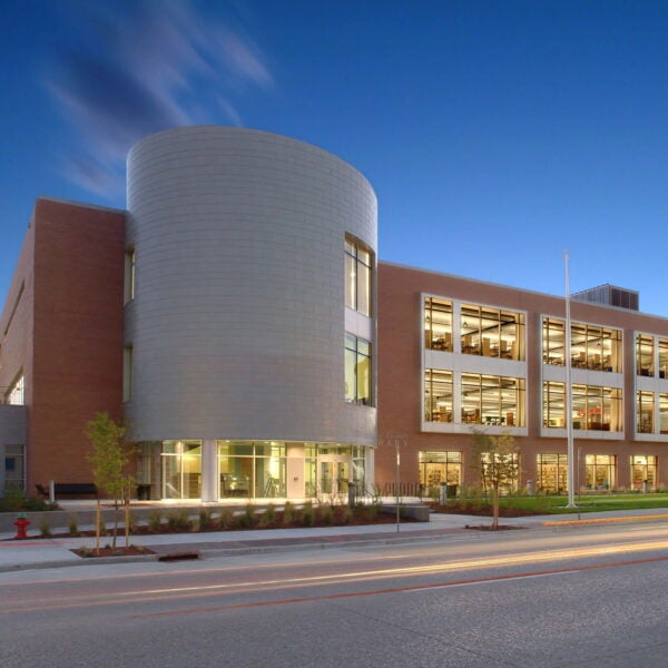 Exterior view of the library’s rounded metal and brick facade illuminated at twilight, with light trails from passing cars.