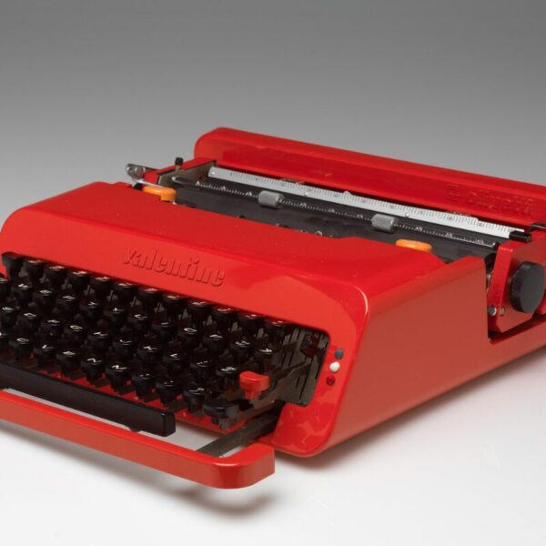 Bright red Olivetti “Valentine” typewriter with black keys and a sleek, modern plastic casing, shown angled on a white surface.