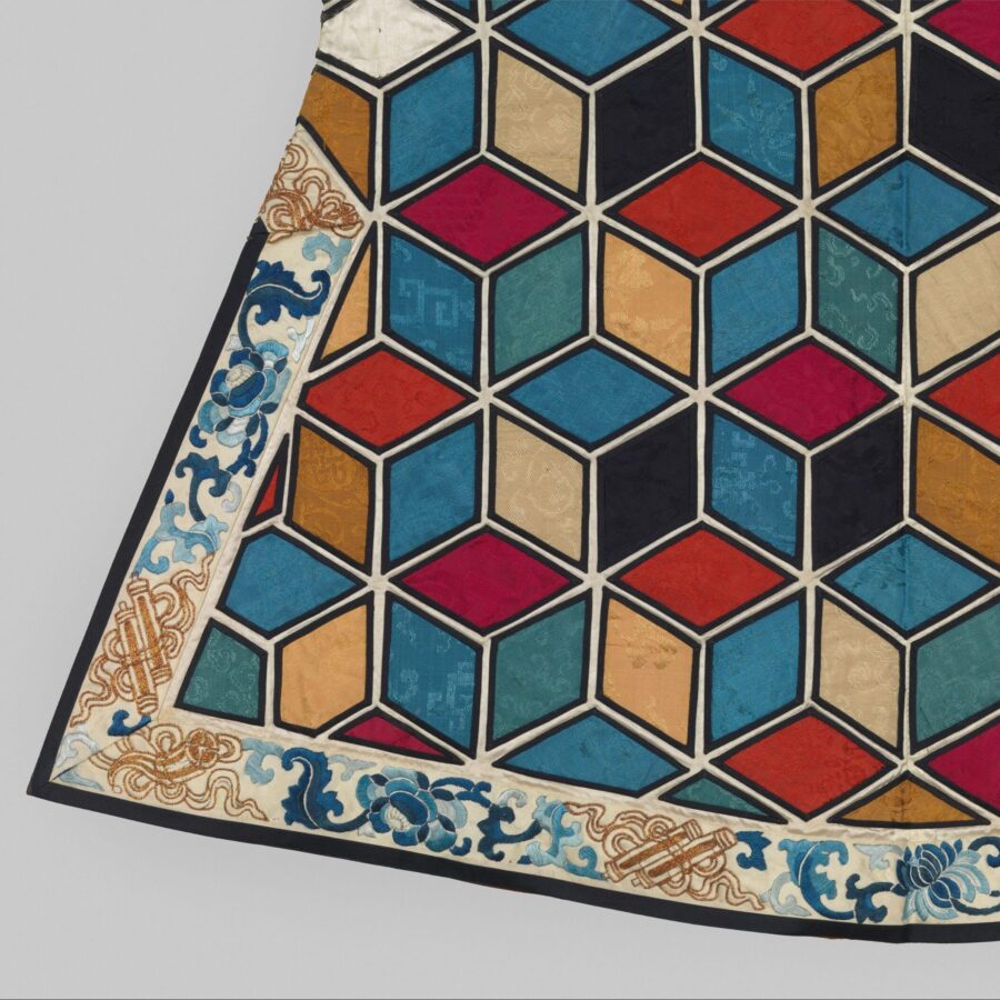 Detail of a textile with colorful, interlocking cube patterns bordered by blue floral and scroll designs.