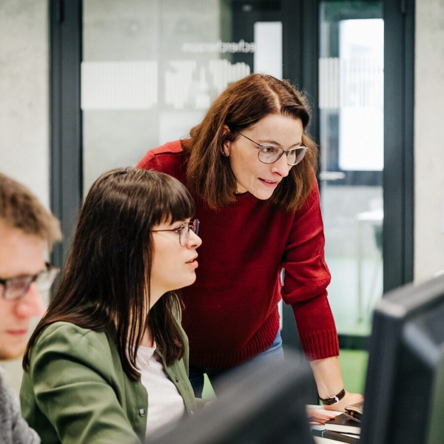 Two colleagues collaborating at a computer in a modern office, reviewing information on a screen together.