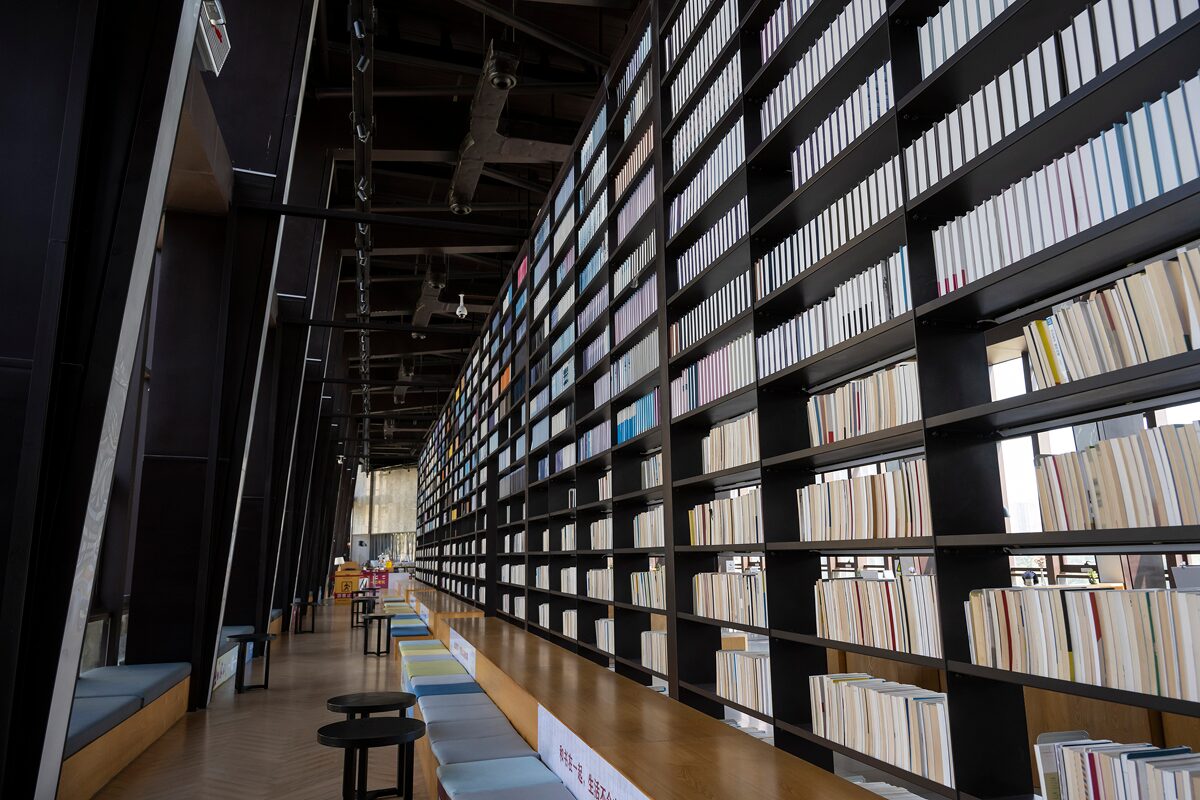 Tall bookshelves filled with colorful books line a modern library interior with natural light.