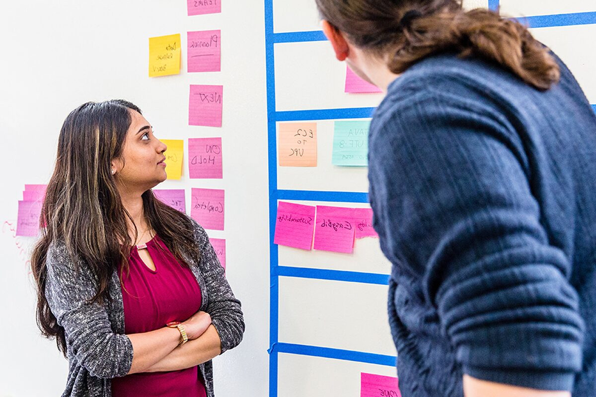Two colleagues standing near a wall of colorful sticky notes, engaged in discussion during a planning session.