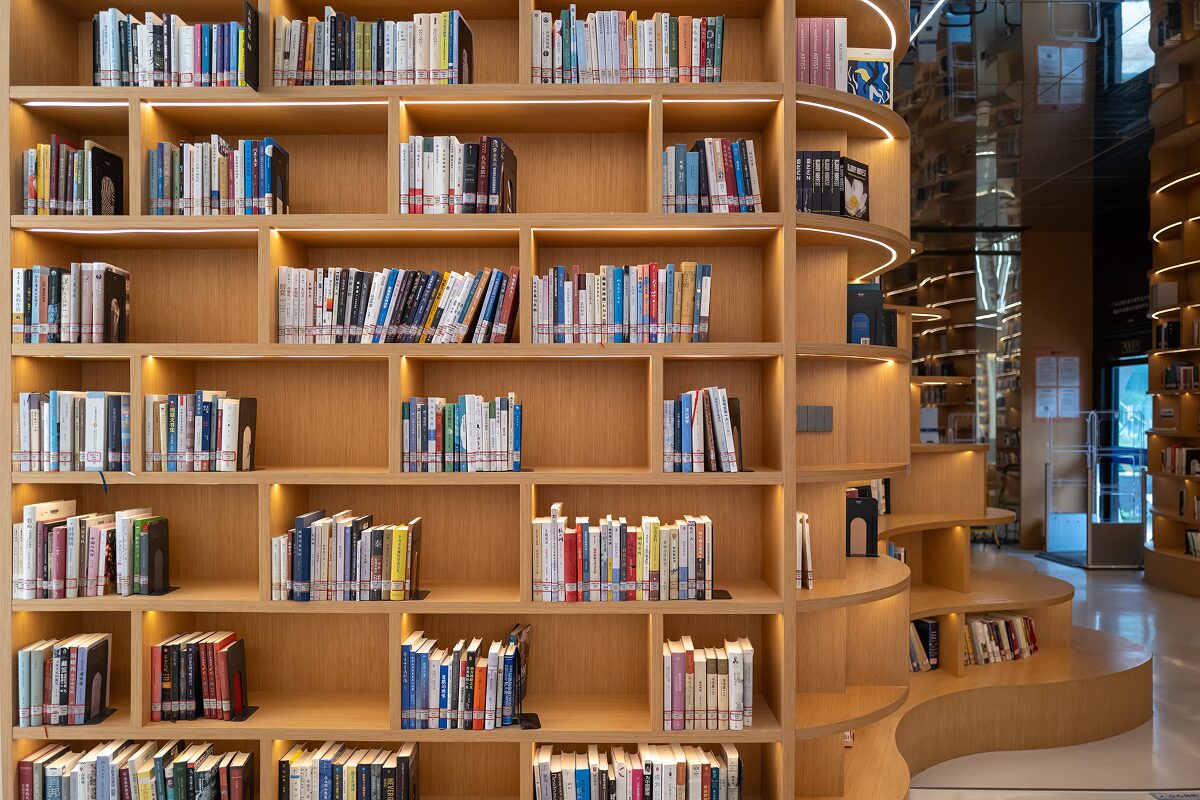 Curved wooden bookshelves filled with neatly arranged books in a warmly lit modern library.