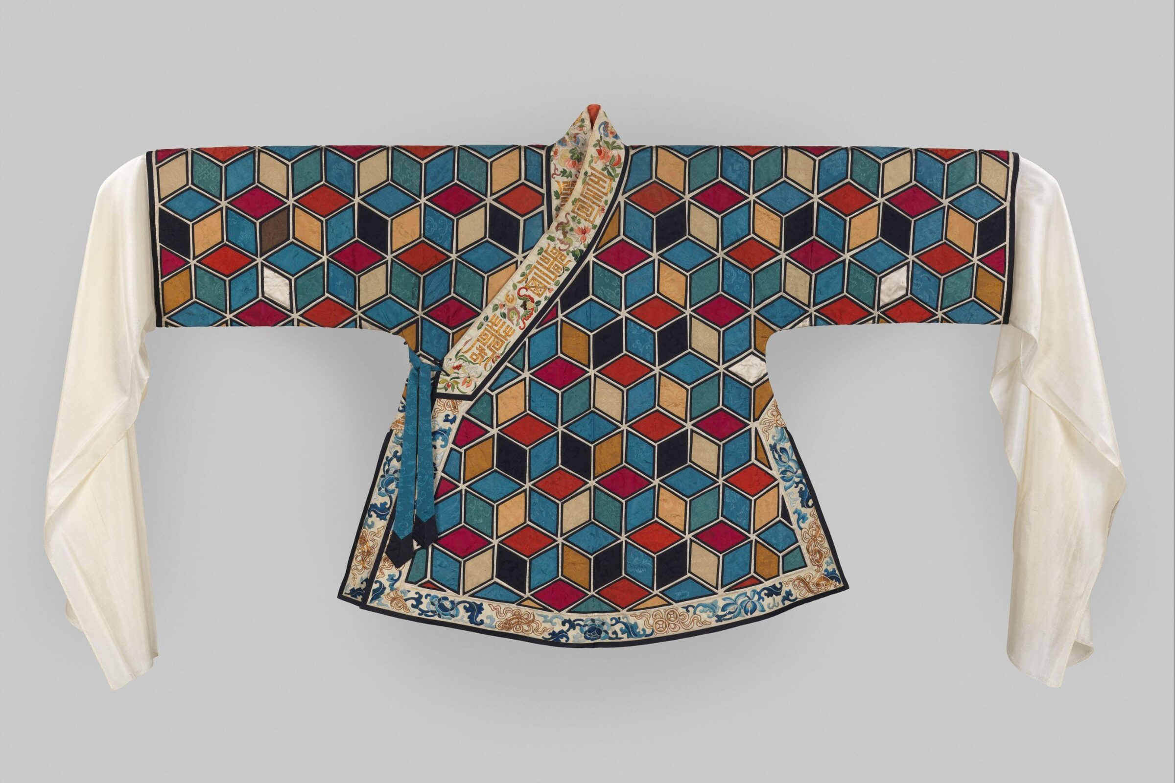 A 19th-century Chinese woman’s theatrical jacket with long white silk sleeves and a body covered in multicolored hexagonal patterns resembling 3D cubes, bordered with embroidered floral designs.