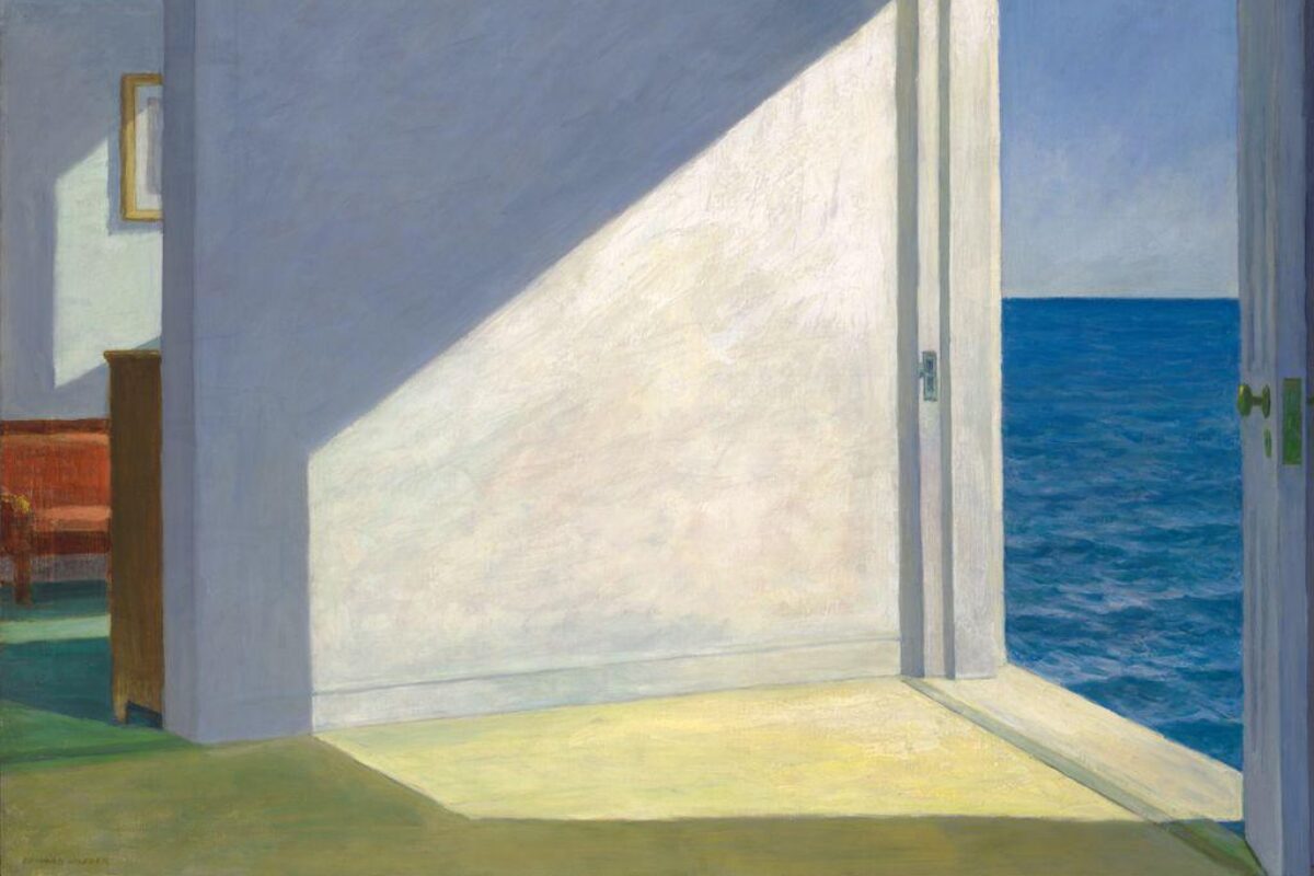 A sunlit room with an open doorway leading to a view of the blue ocean, casting strong geometric shadows across the interior floor and walls.