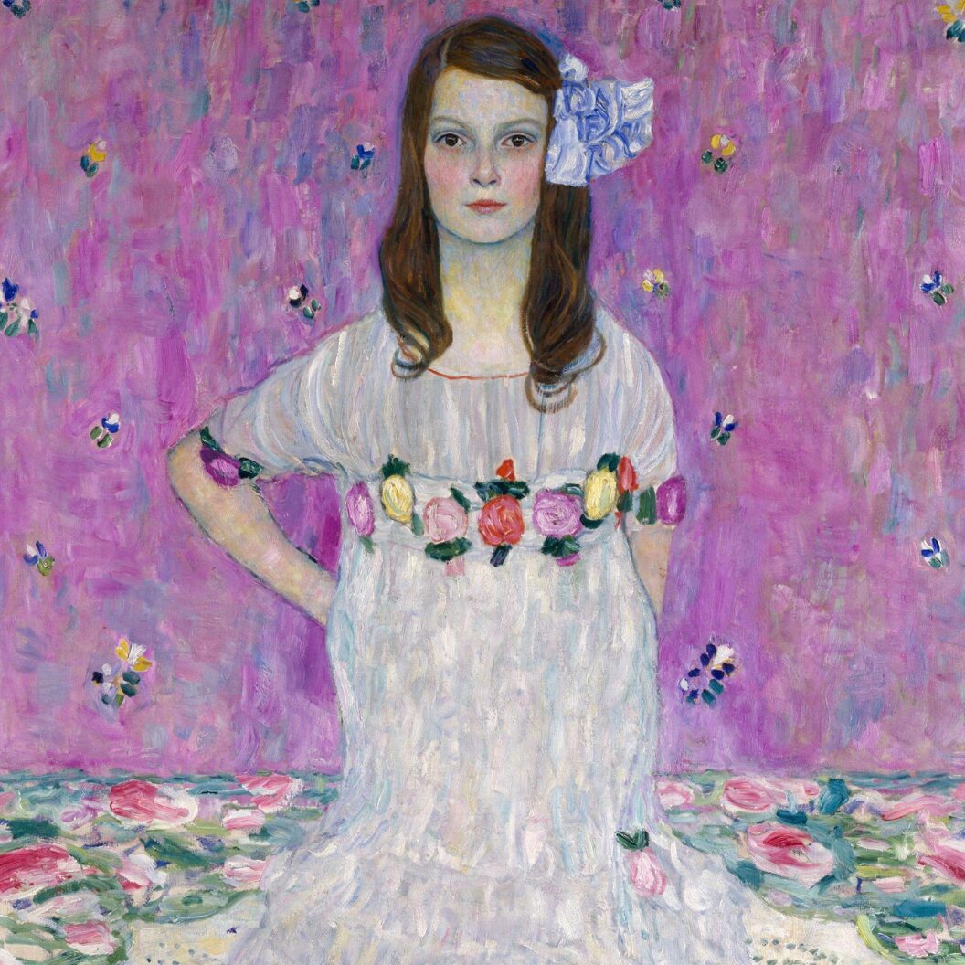 A full-length portrait of a young girl in a ruffled white dress standing confidently against a bright pink, patterned background.