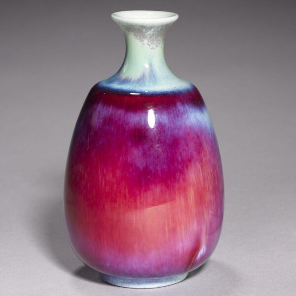 Small ceramic vase with a rounded body and narrow neck, glazed in gradients of deep purple, magenta, and blue against a gray background.