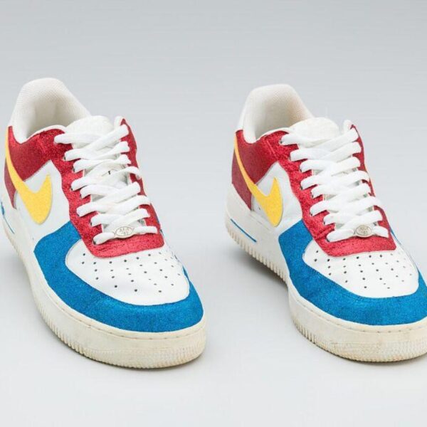 A pair of Nike sneakers in white with bright red, blue, and yellow suede panels, shown from the front.