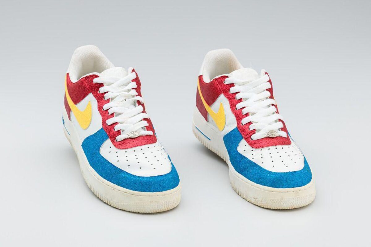 A pair of Nike sneakers in white with bright red, blue, and yellow suede panels, shown from the front.
