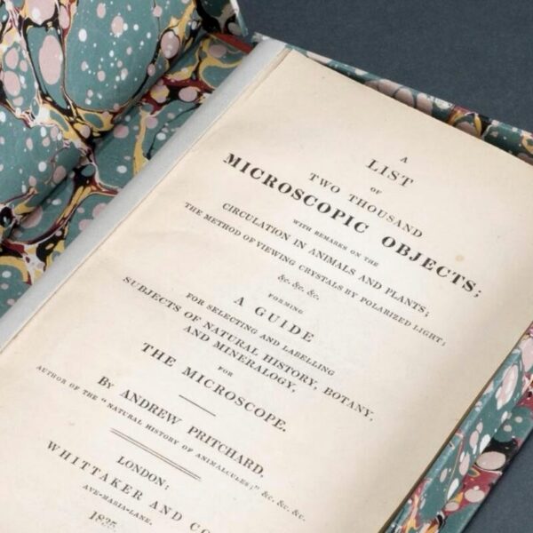 Open book titled A List of Two Thousand Microscopic Objects displayed in a marbled slipcase, showing its printed title page with detailed text by Andrew Pritchard.