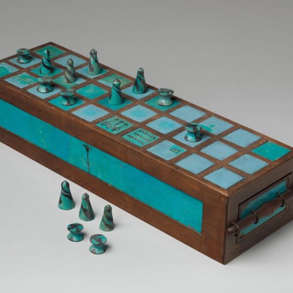 An ancient Egyptian game board made of wood and turquoise-colored inlays, with conical and spool-shaped playing pieces arranged on top and several pieces placed in front.